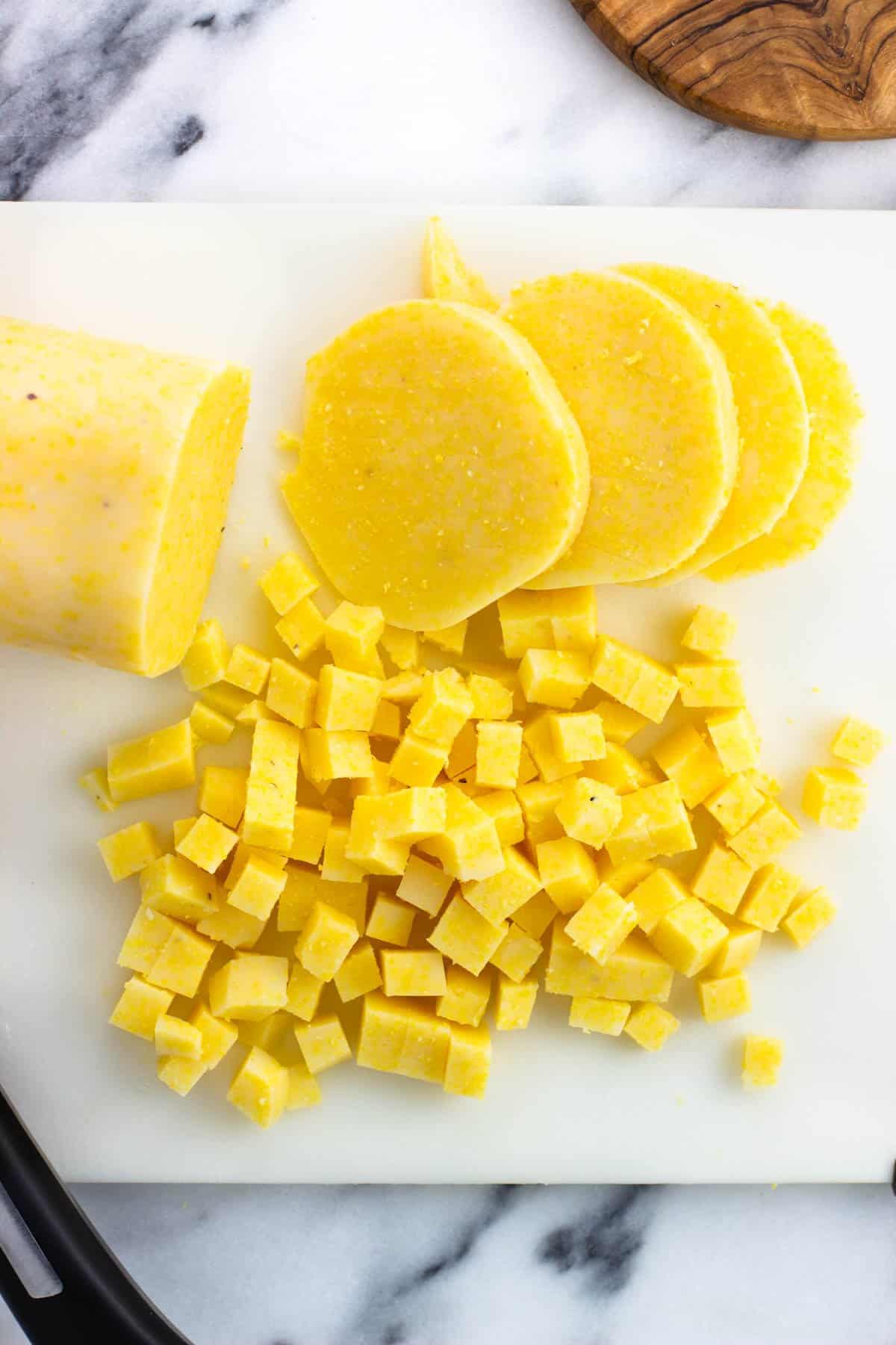 A tube of polenta being chopped into small cubes.