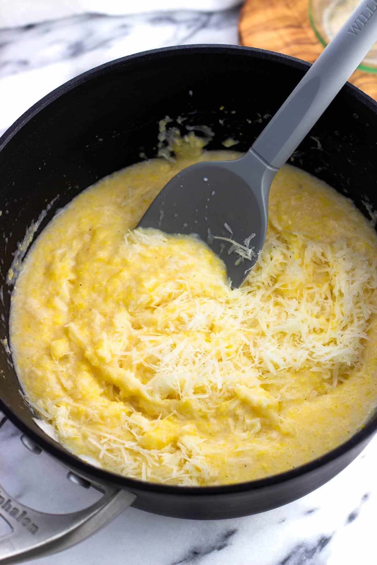 Grated Parmesan being stirred into the pot of polenta.