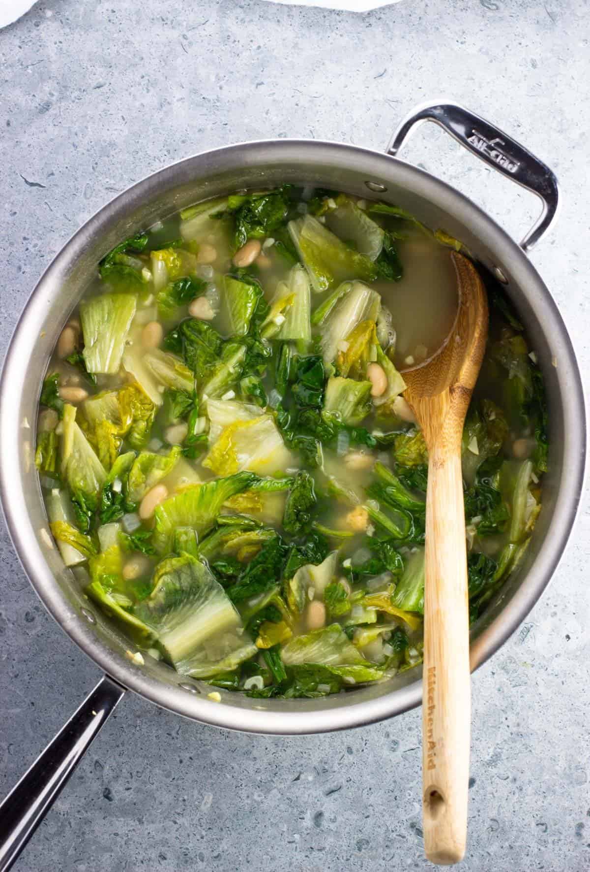 Well-simmered escarole and beans in a pot with a wooden spoon.