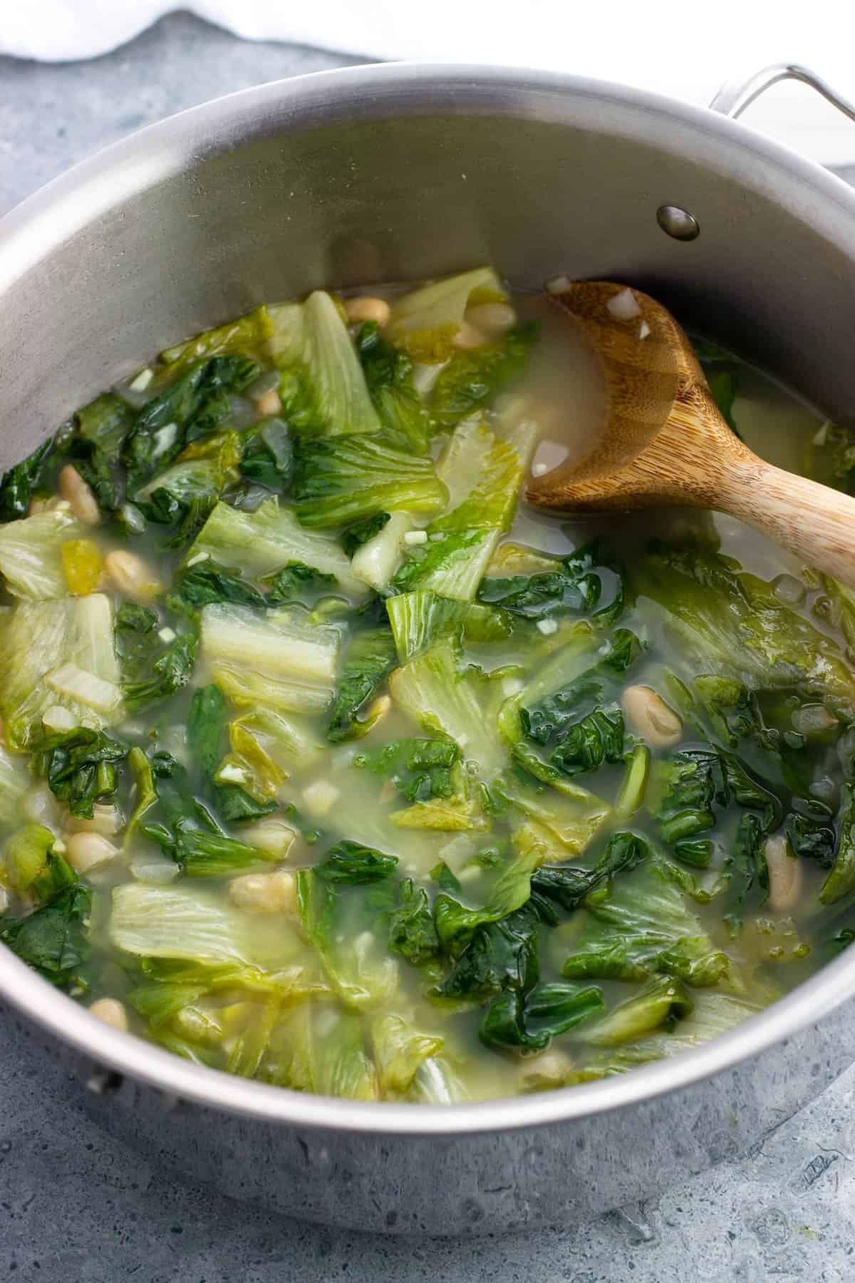 A wooden spoon in a large pot of escarole and bean soup.