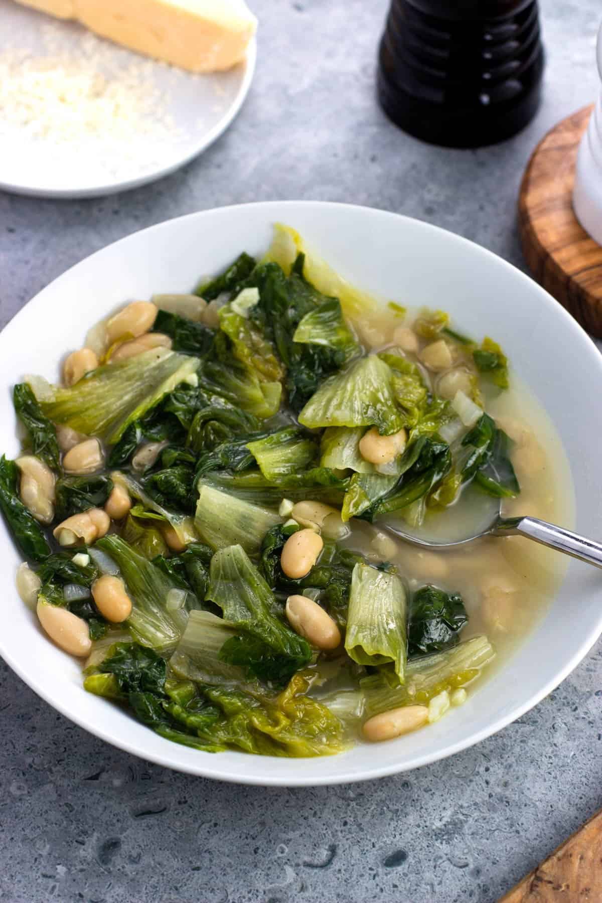 A shallow bowl of brothy escarole and beans with a soup spoon.