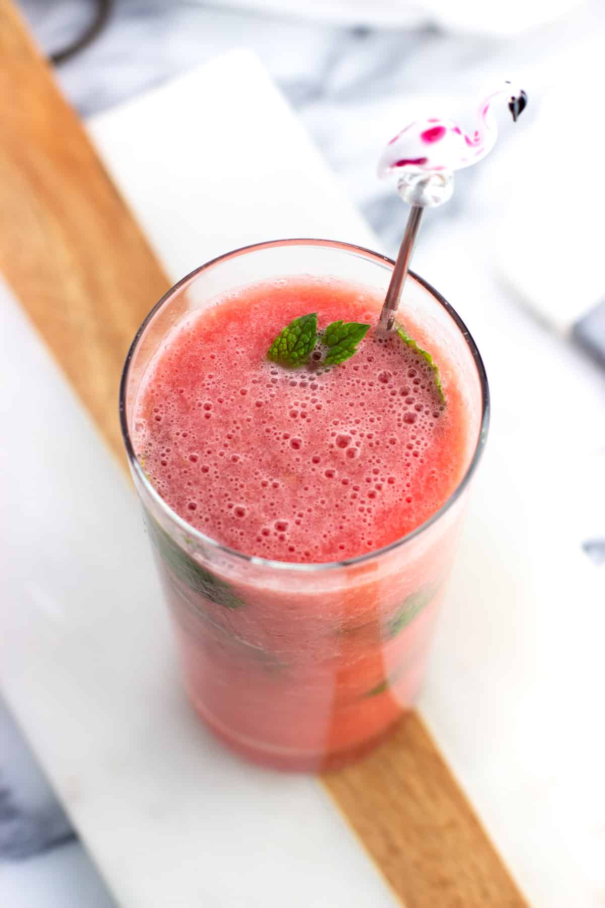 A watermelon mocktail in a tall glass garnished with mint and a flamingo drink stirrer.
