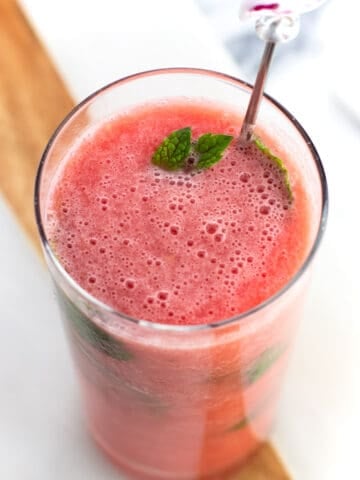 A watermelon mocktail in a tall glass garnished with mint and a flamingo drink stirrer.