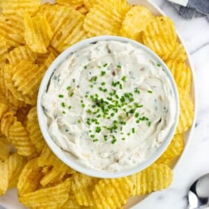 A serving tray of sour cream and onion dip and wavy chips.