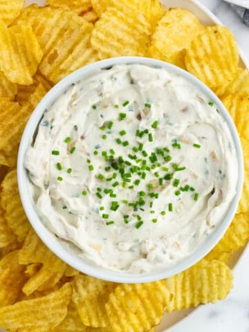 A serving tray of sour cream and onion dip and wavy chips.