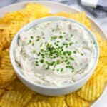 Sour cream and onion dip in a serving bowl with wavy chips around it.