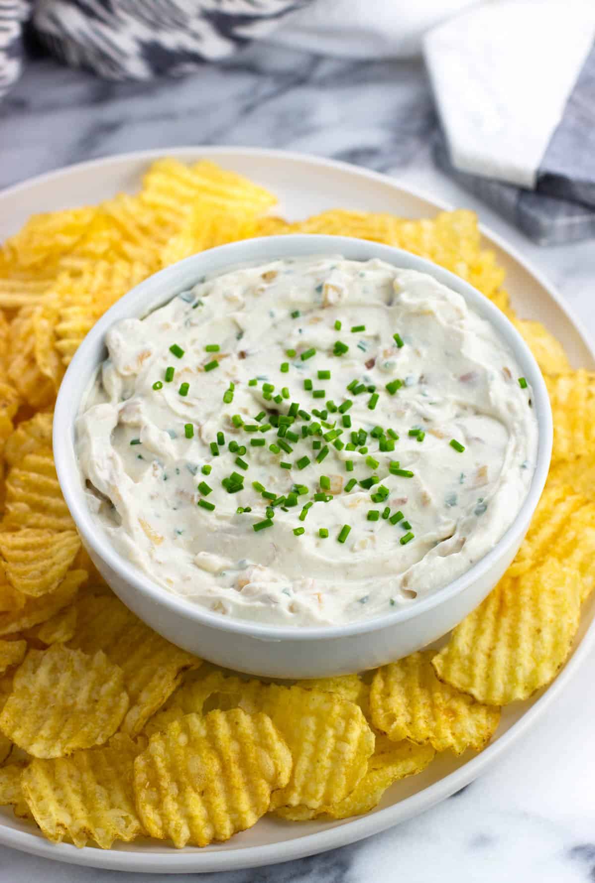 Sour cream and onion dip in a serving bowl with wavy chips around it.