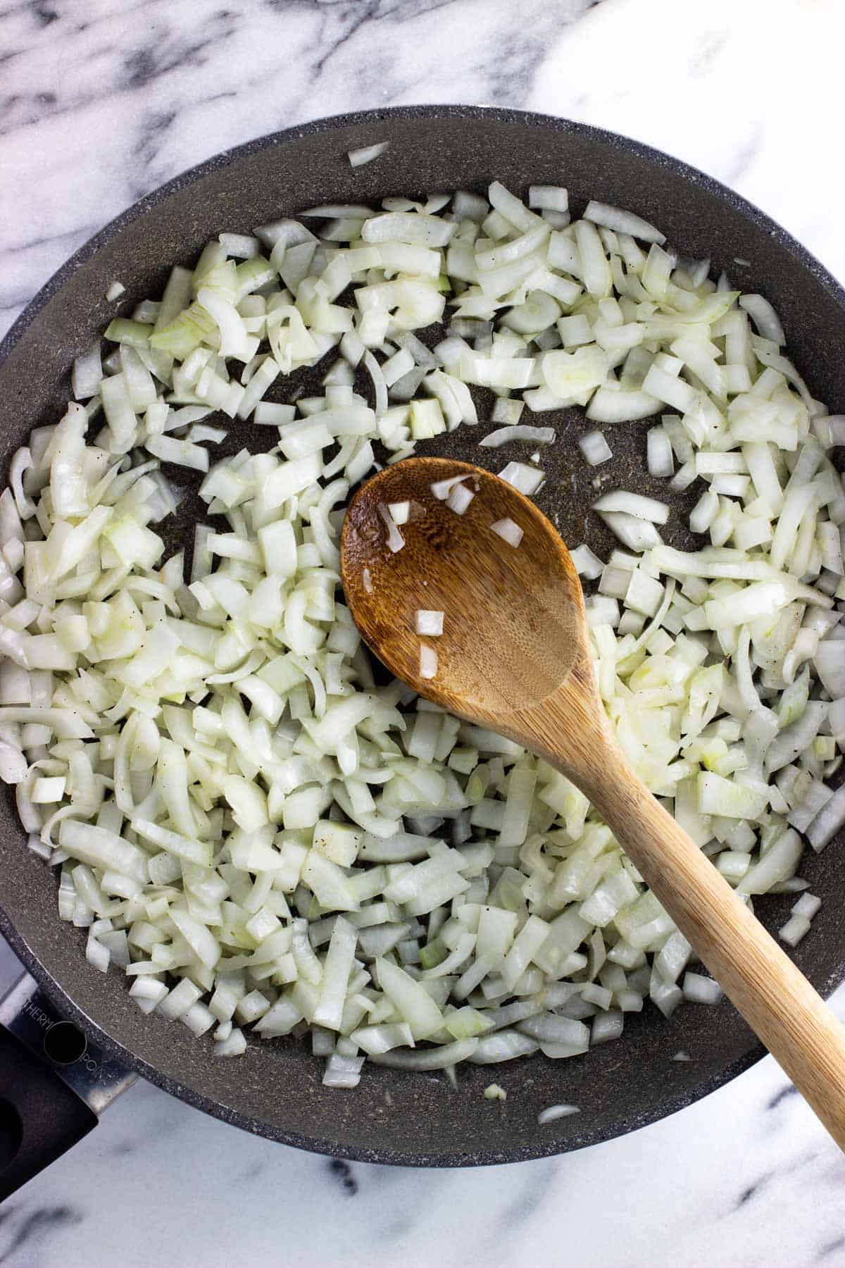 Diced onion pieces in a pan with a wooden spoon.
