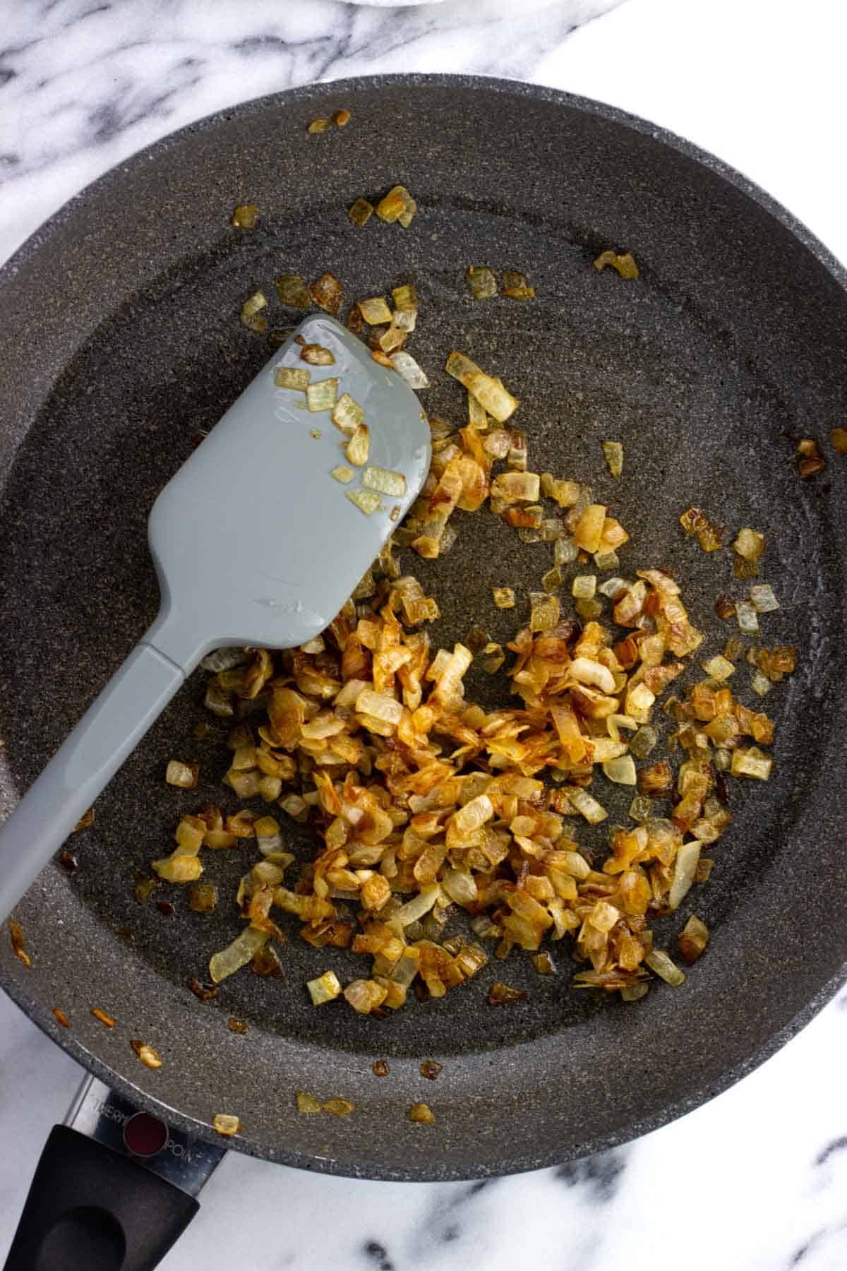 Caramelized diced onion in a pan with a spatula.