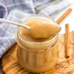 A spoon of applesauce resting on a jar of it.