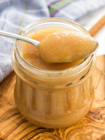 A spoon full of applesauce resting on the jar of it.