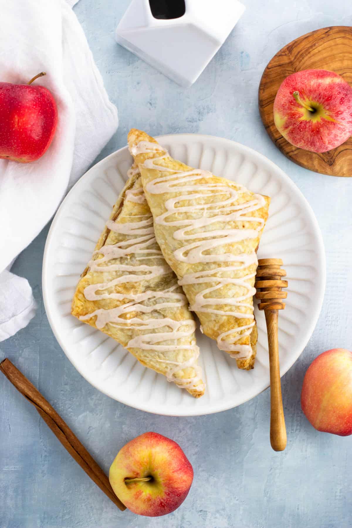 Two apple turnovers on a plate drizzled with cinnamon glaze.