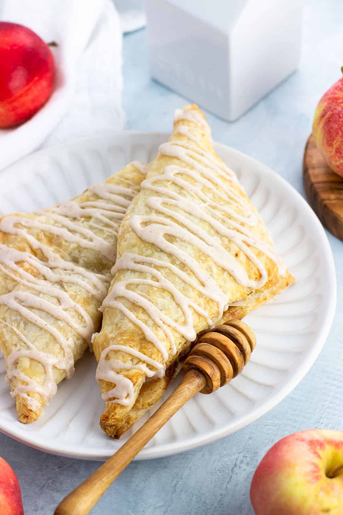 Two apple turnovers on a plate drizzled with cinnamon glaze.