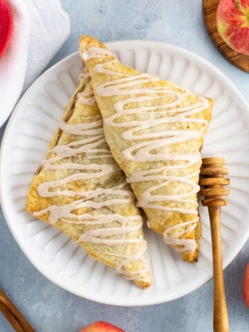 Two apple turnovers on a plate drizzled with cinnamon glaze.