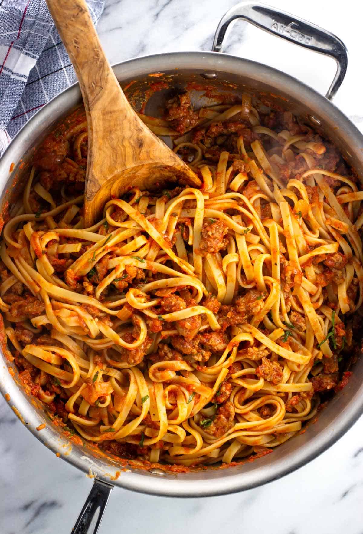 A pan of sausage fettuccine mixed together with a wooden spoon.