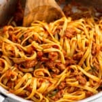 A pan of sausage fettuccine mixed together with a wooden spoon.