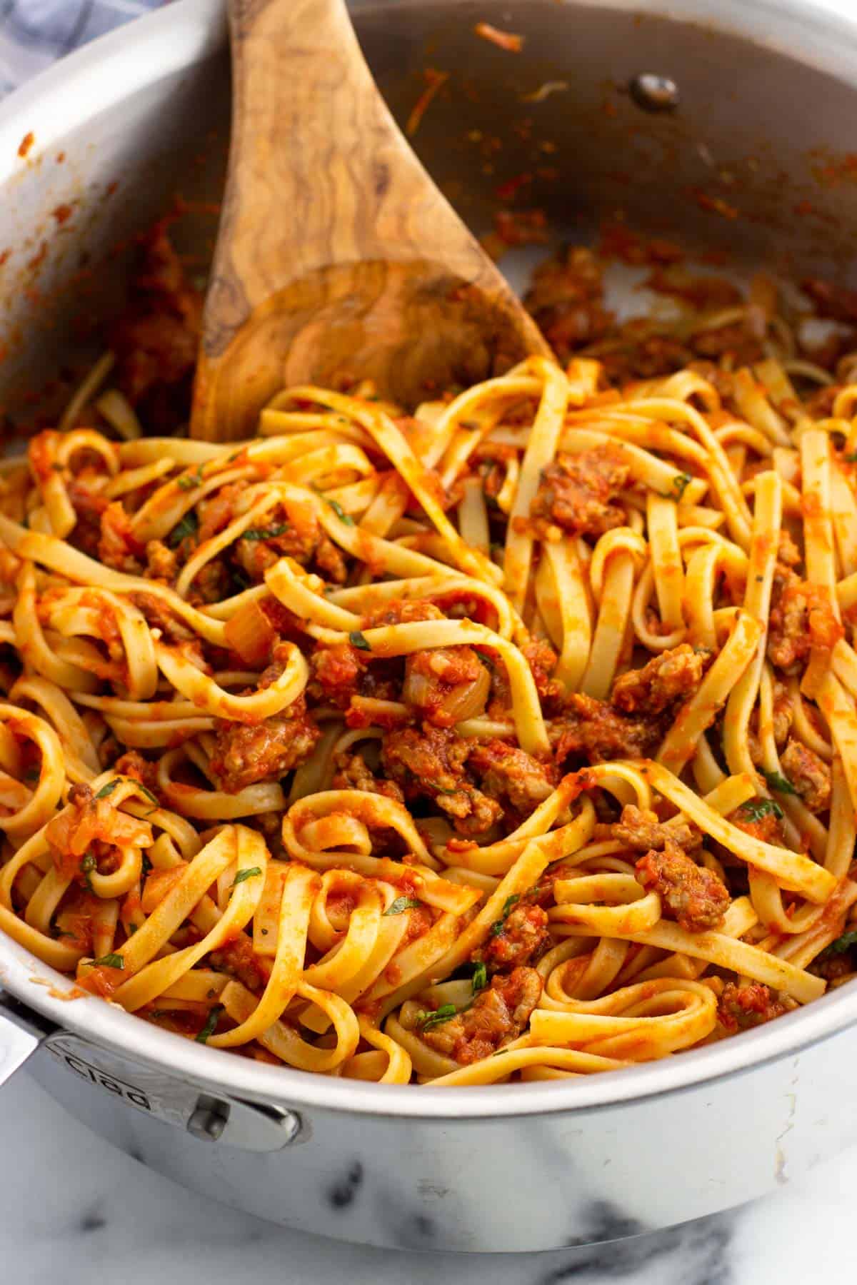 A pan of sausage fettuccine mixed together with a wooden spoon.