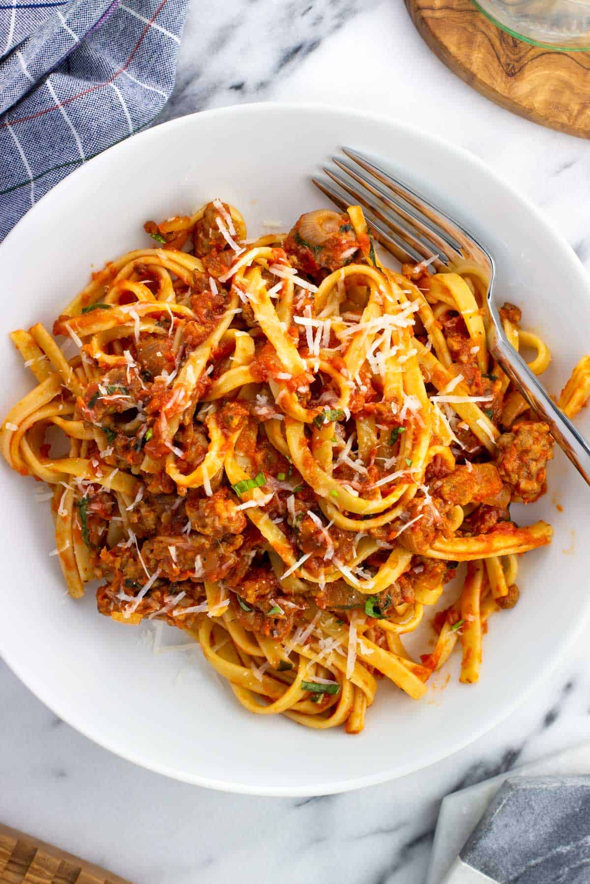 A plate of spicy sausage fettuccine with a fork topped with Parmesan.