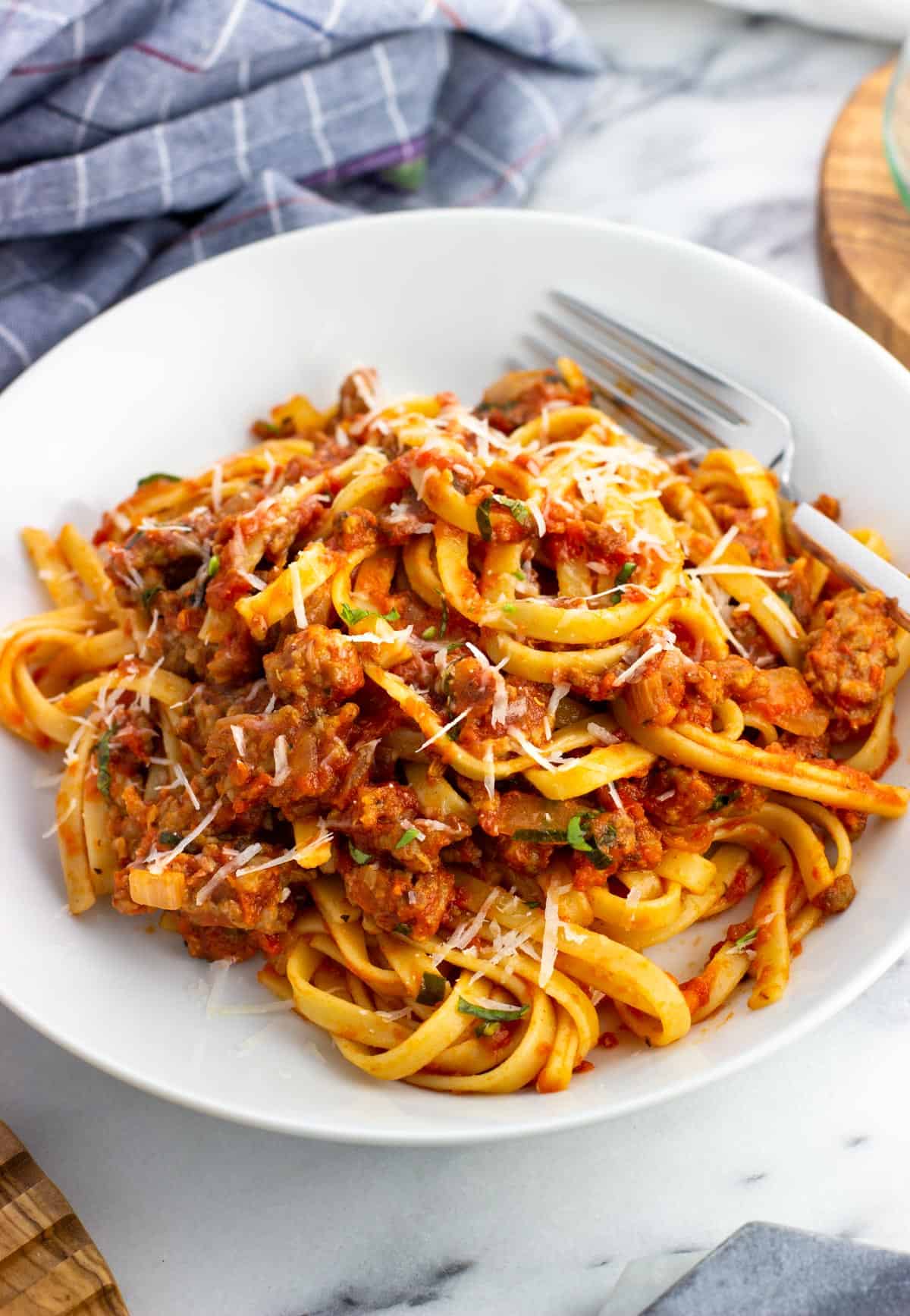 A plate of spicy sausage fettuccine with a fork topped with Parmesan.