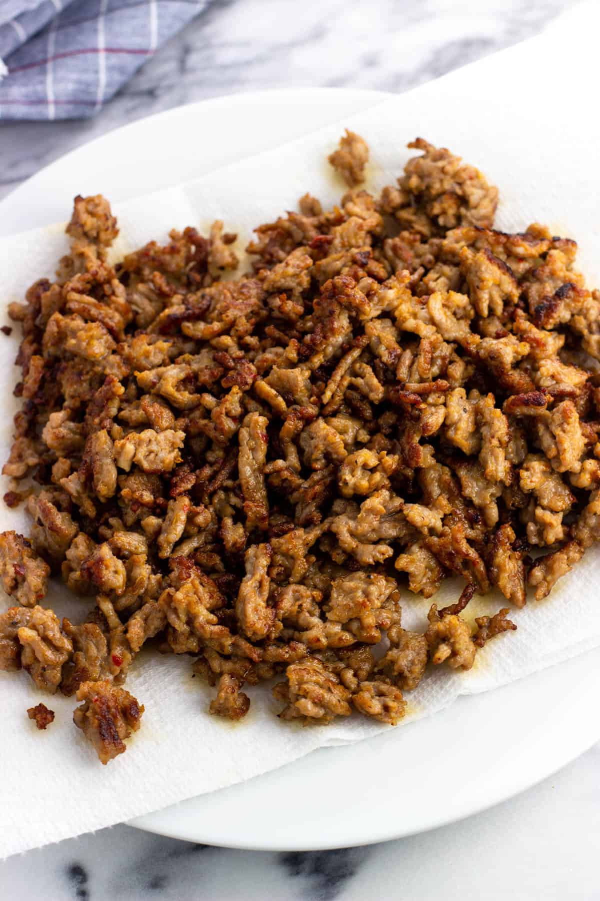 Cooked and crumbled Italian sausage on a paper towel-lined plate.