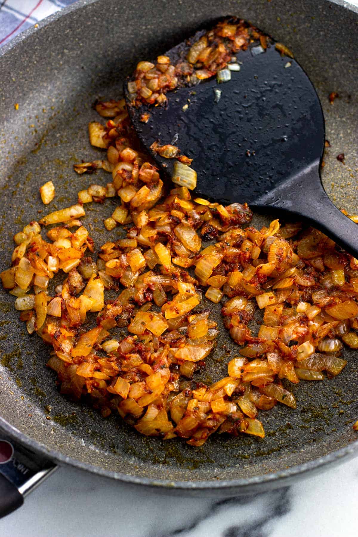 Sauteed onion, garlic, and tomato paste in a pan with a spatula.