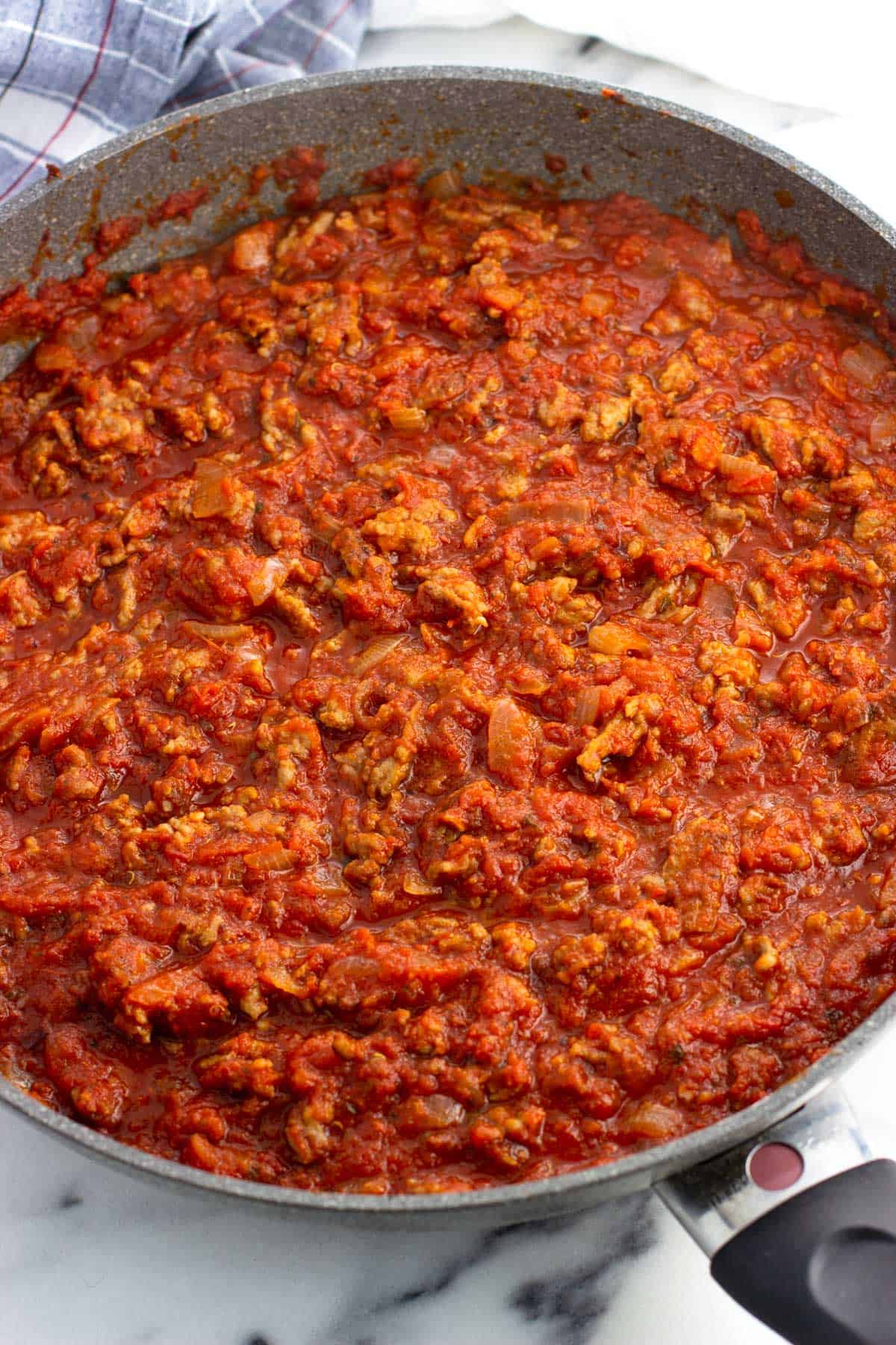 Crushed tomatoes and spices added to the pan to form a sauce.