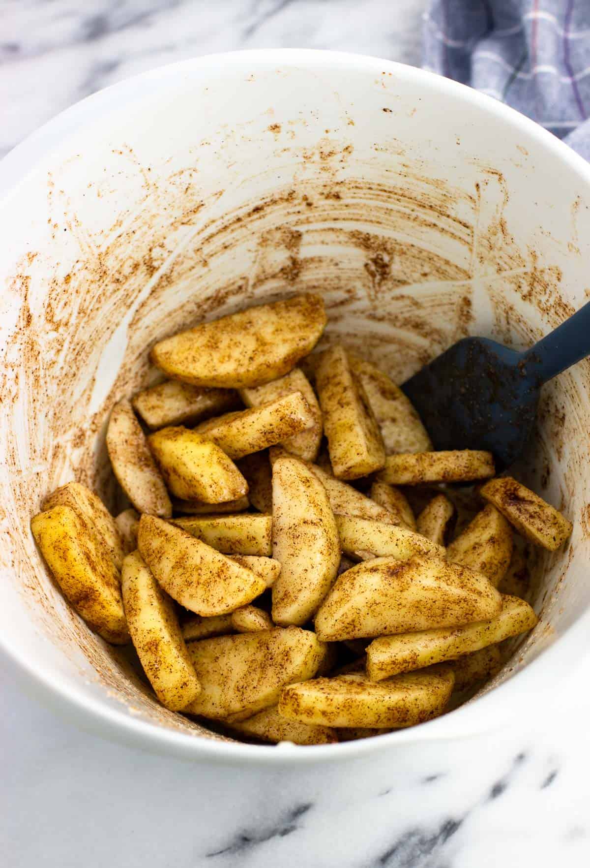 Raw apple slices coated with oil, sugar, and spices in a mixing bowl.