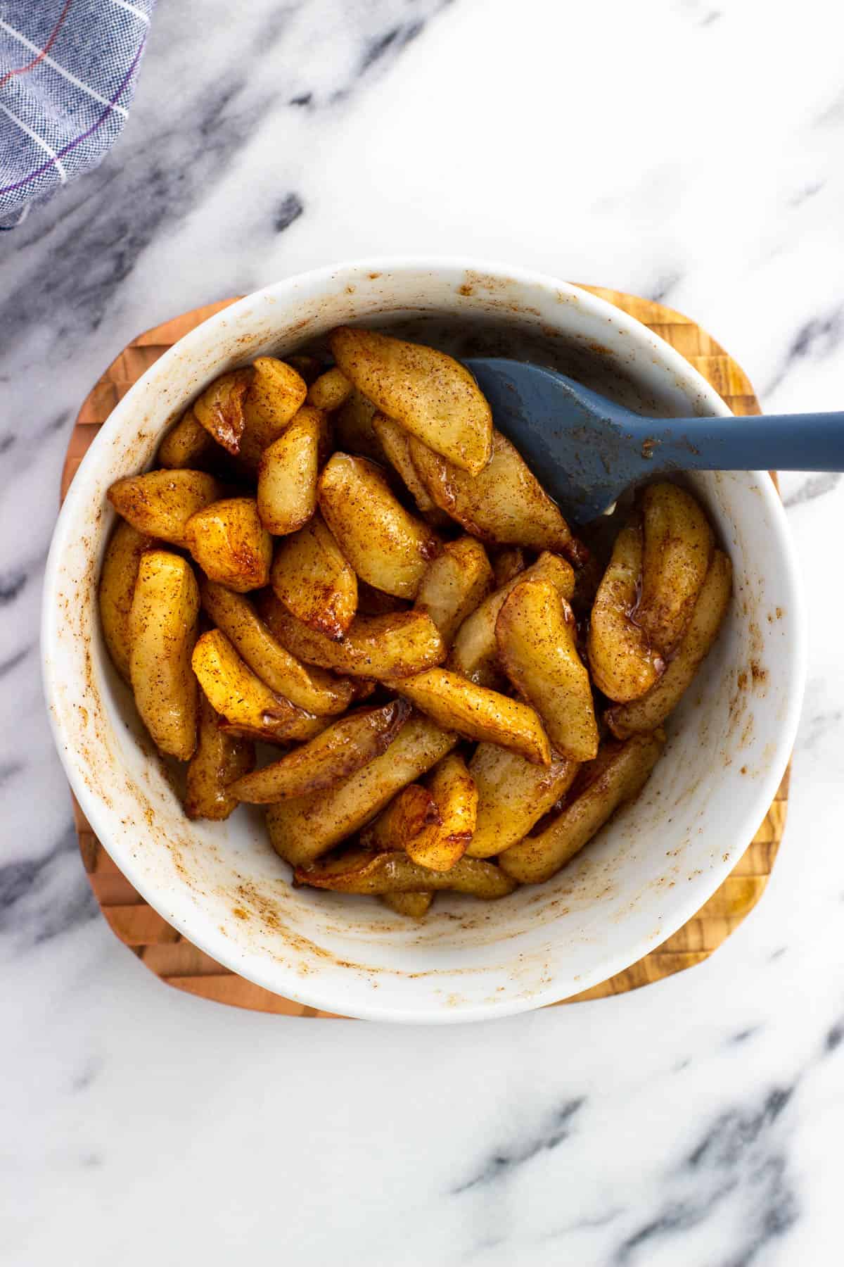 Apple slices coated with butter and brown sugar in a bowl with a spatula.