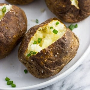 A close-up of an air fryer baked potato served with a pat of butter and chives.