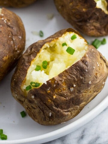 A close-up of an air fryer baked potato served with a pat of butter and chives.
