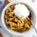A bowl of apple crumble served with a scoop of vanilla ice cream.