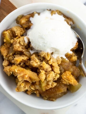 A bowl of apple crumble served with a scoop of vanilla ice cream.