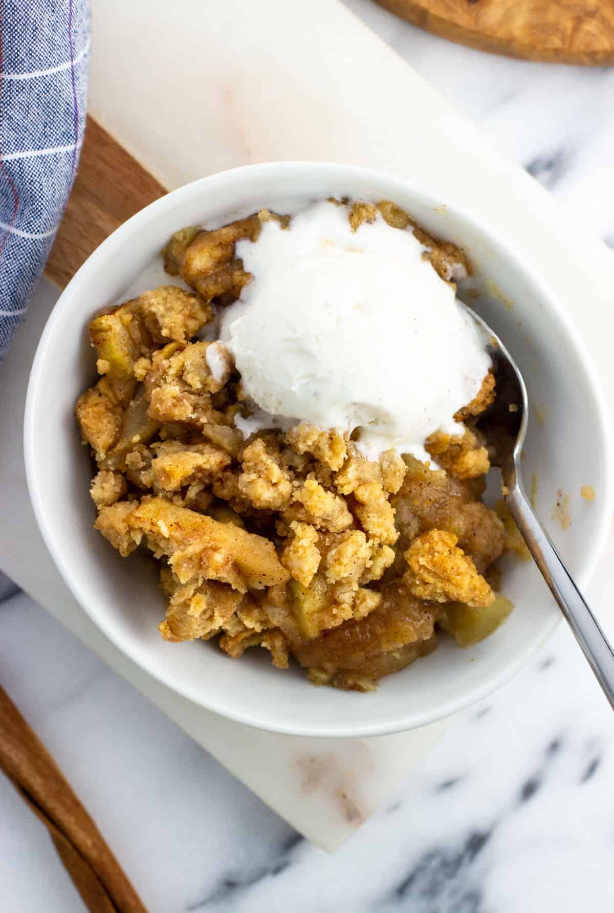 A bowl of apple crumble served with a scoop of vanilla ice cream.