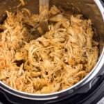 Shredded buffalo chicken in the Instant Pot with a serving spoon.
