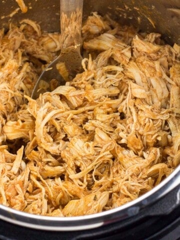 Shredded buffalo chicken in the Instant Pot with a serving spoon.