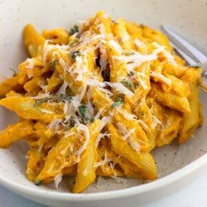 A serving of pumpkin pasta in a bowl topped with grated Pecorino and sage.