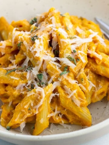 A serving of pumpkin pasta in a bowl topped with grated Pecorino and sage.