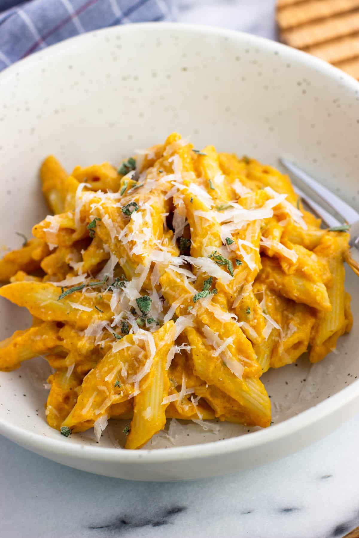 A serving of pumpkin pasta in a bowl topped with grated Pecorino and sage.