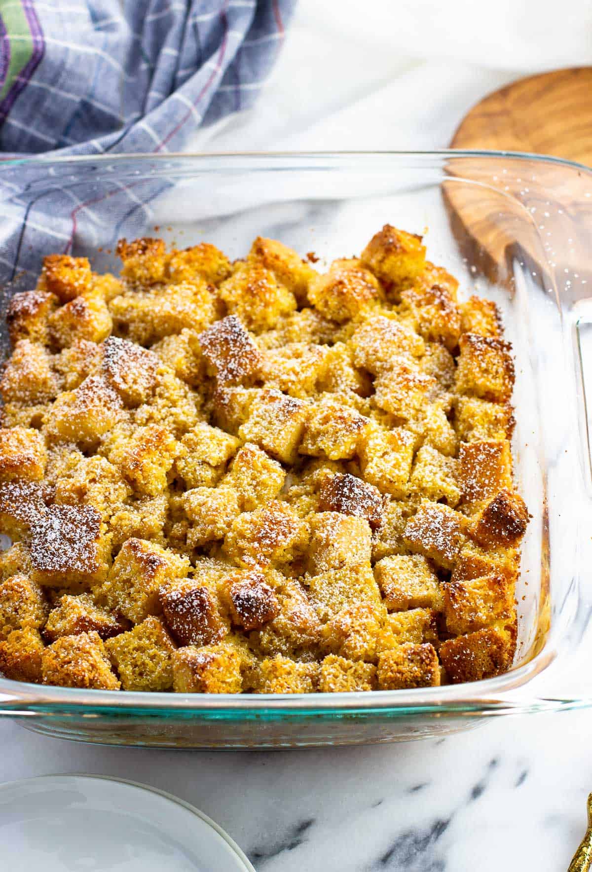 Baked cornbread french toast in a square pan topped with powdered sugar.