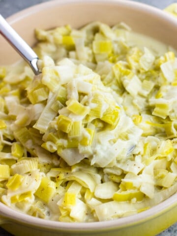 A spoon lifting up a scoop of creamed leeks from a serving dish.