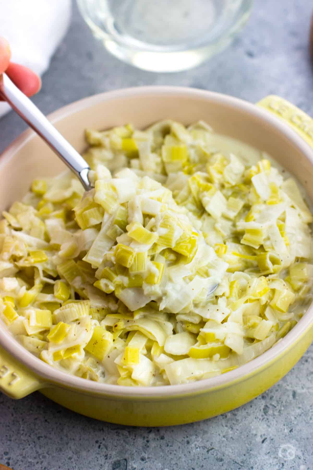 A spoon lifting up a scoop of creamed leeks.