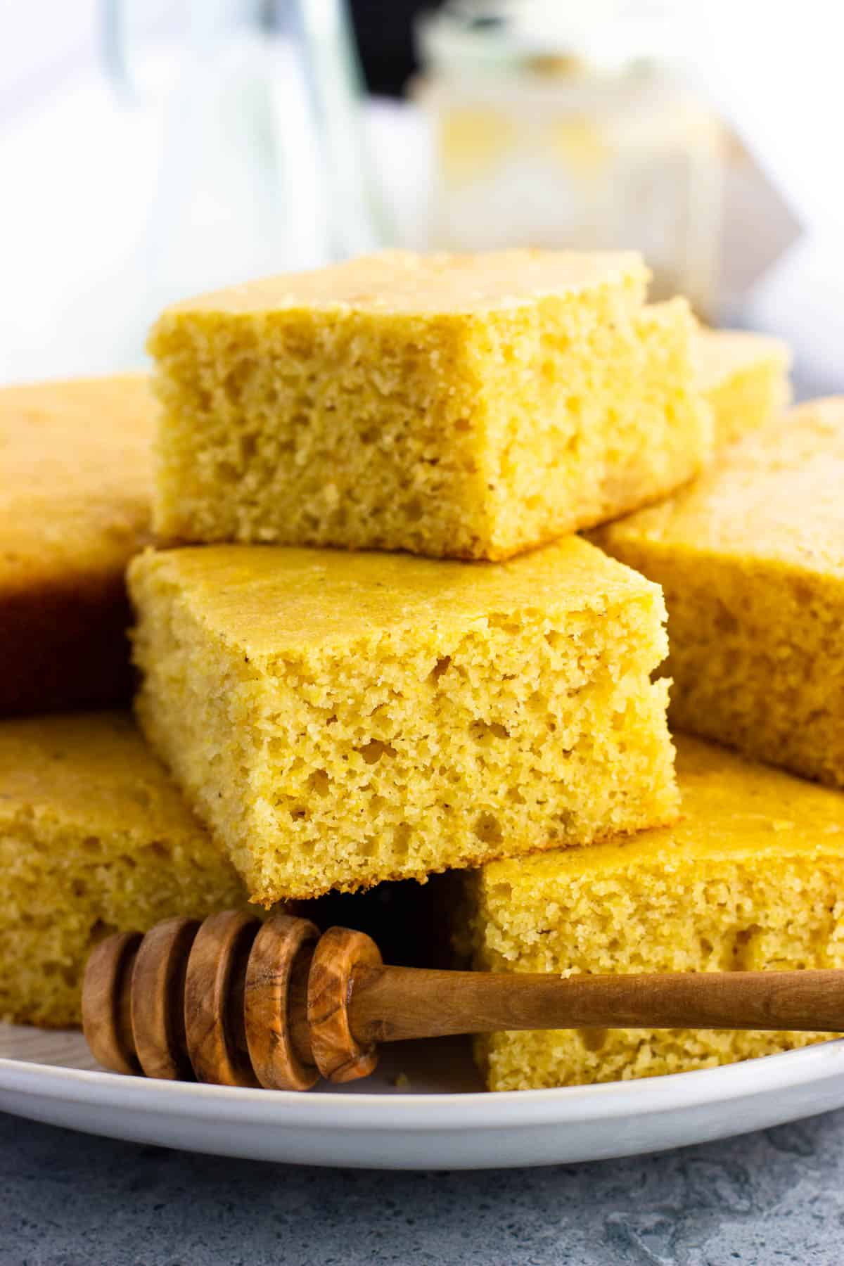 Pieces of honey cornbread stacked on a plate with a wooden honey dipper.