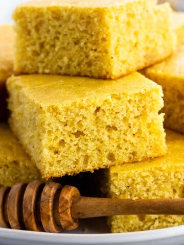 Pieces of honey cornbread stacked on a plate with a wooden honey dipper.