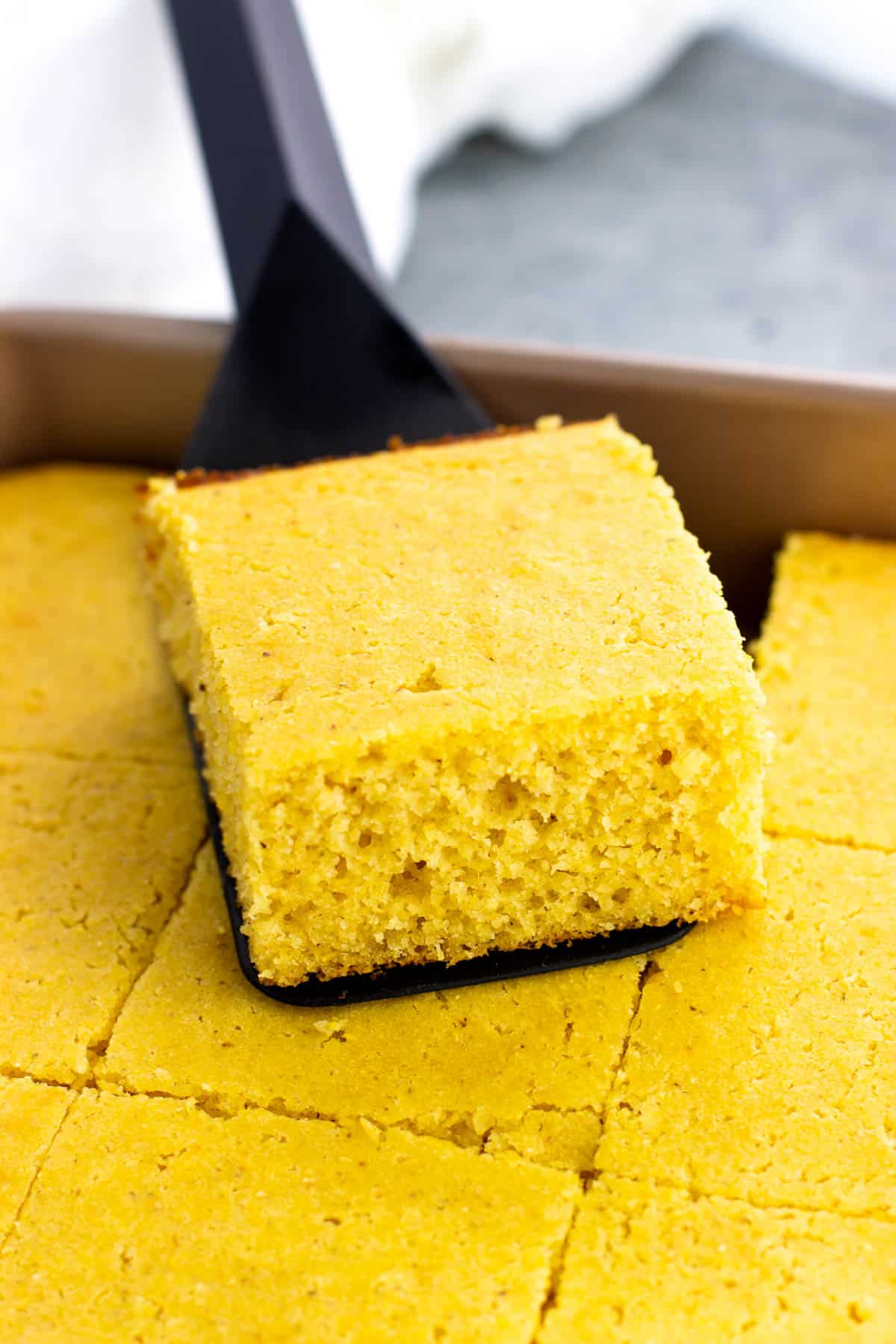 A spatula lifting up a wedge of cornbread on top of the pan.