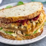 A loaded Thanksgiving turkey sandwich, featuring mashed potatoes, lettuce, gravy, stuffing, and cranberry sauce.