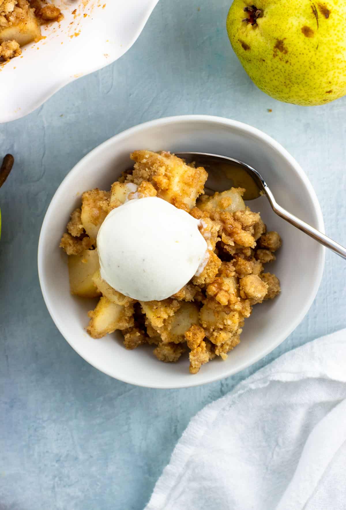 A serving of pear crumble in a bowl topped with a small scoop of melty vanilla ice cream.