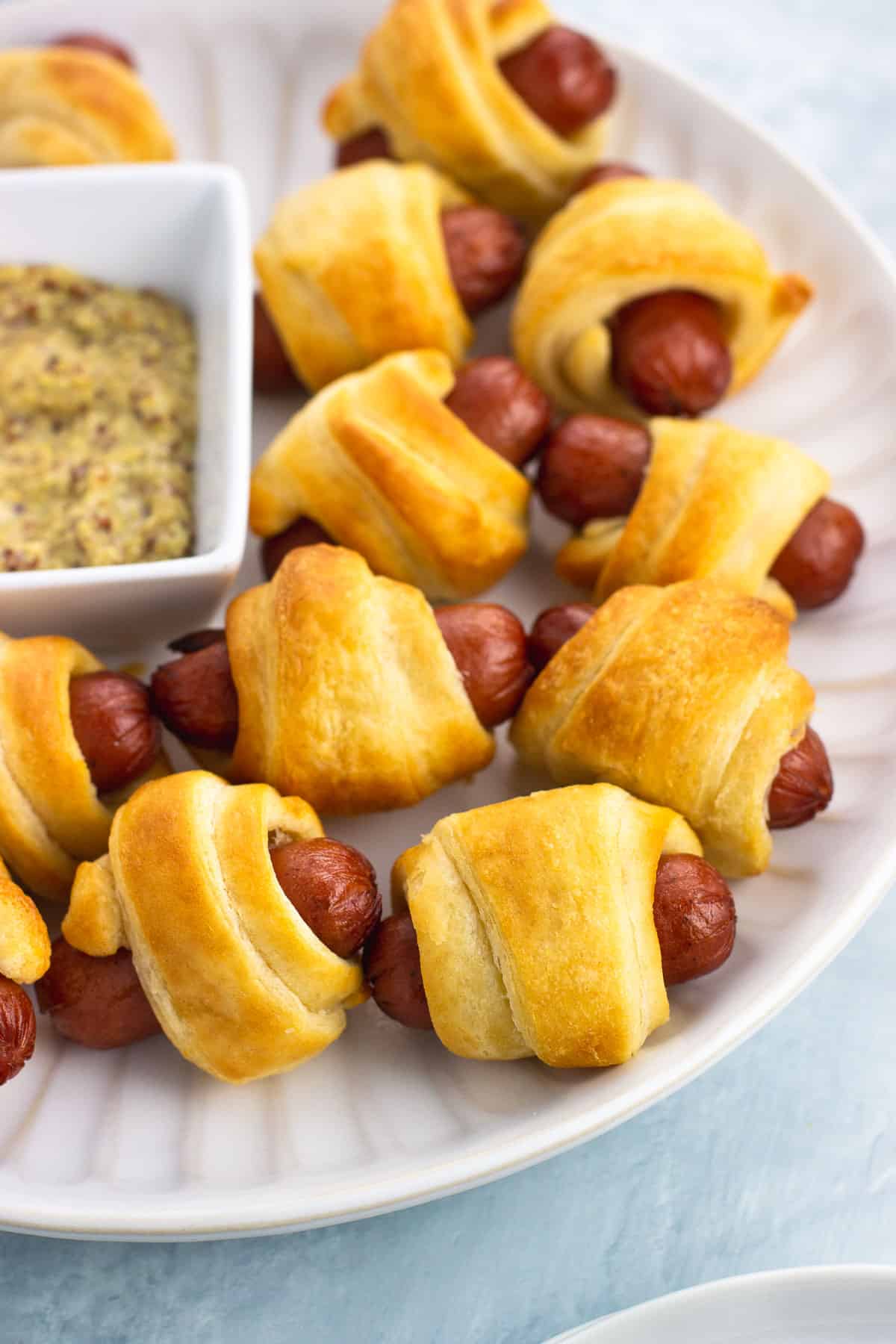 A plate of pigs in a blanket with a small bowl of dipping mustard.