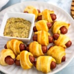 A plate of air fryer pigs in a blanket with a small bowl of dipping mustard.