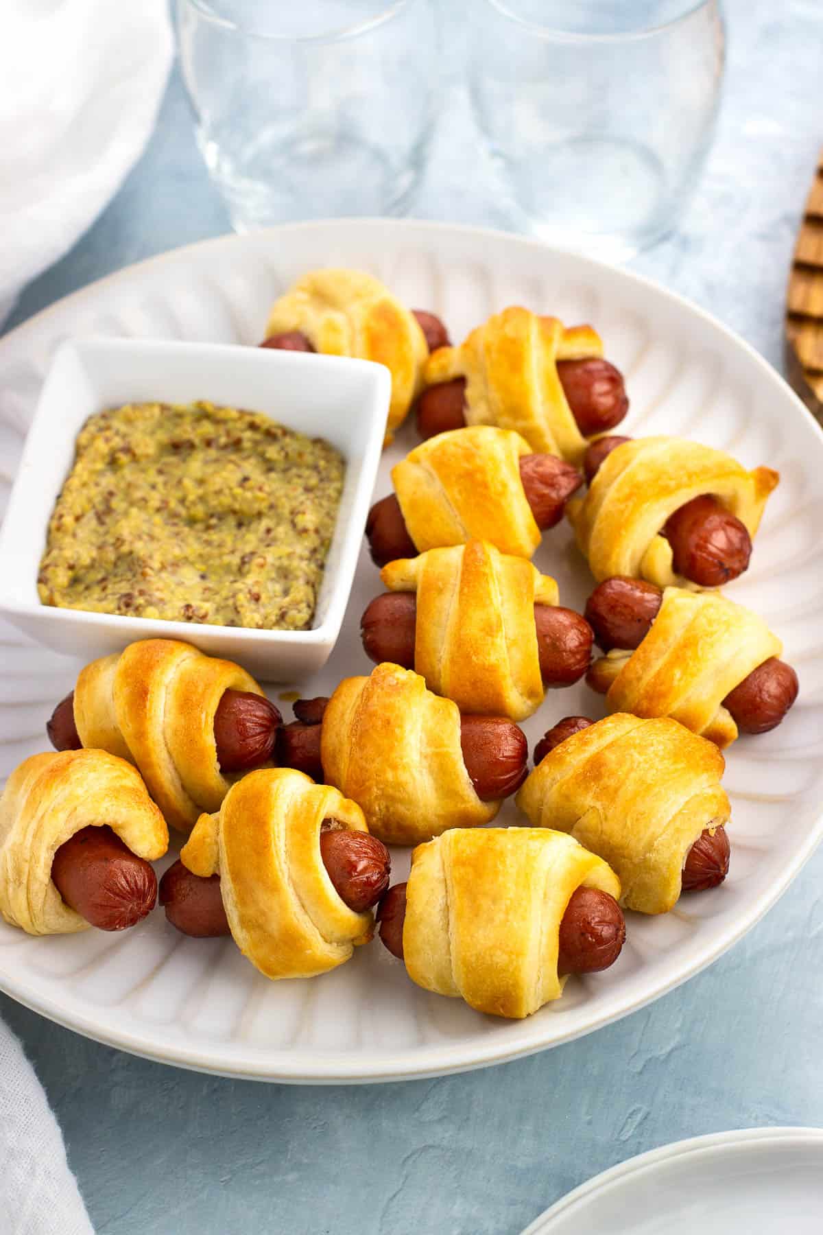 A plate of air fryer pigs in a blanket with a small bowl of dipping mustard.