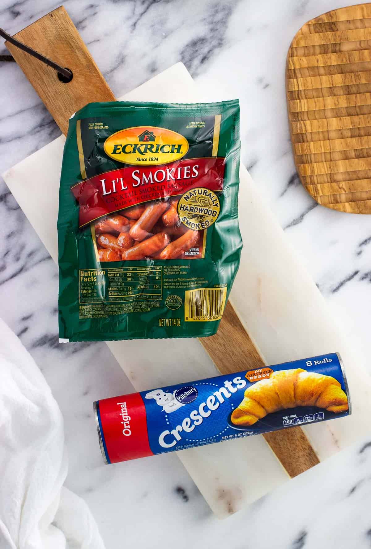 A package of li'l smokies cocktail sausages and a tube of crescent rolls on a marble board.